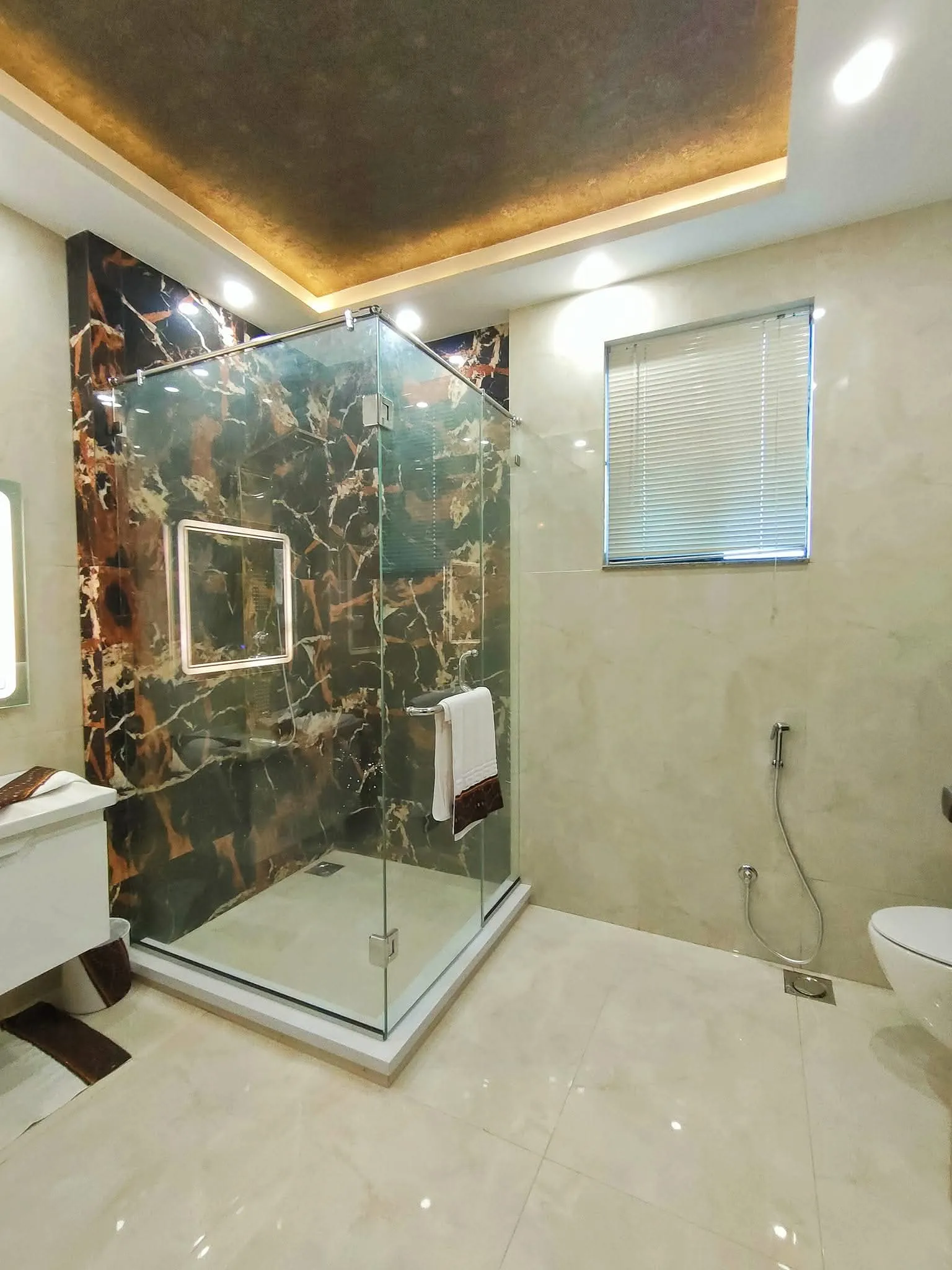 Bathroom finished in green veined marble with a frameless glass shower