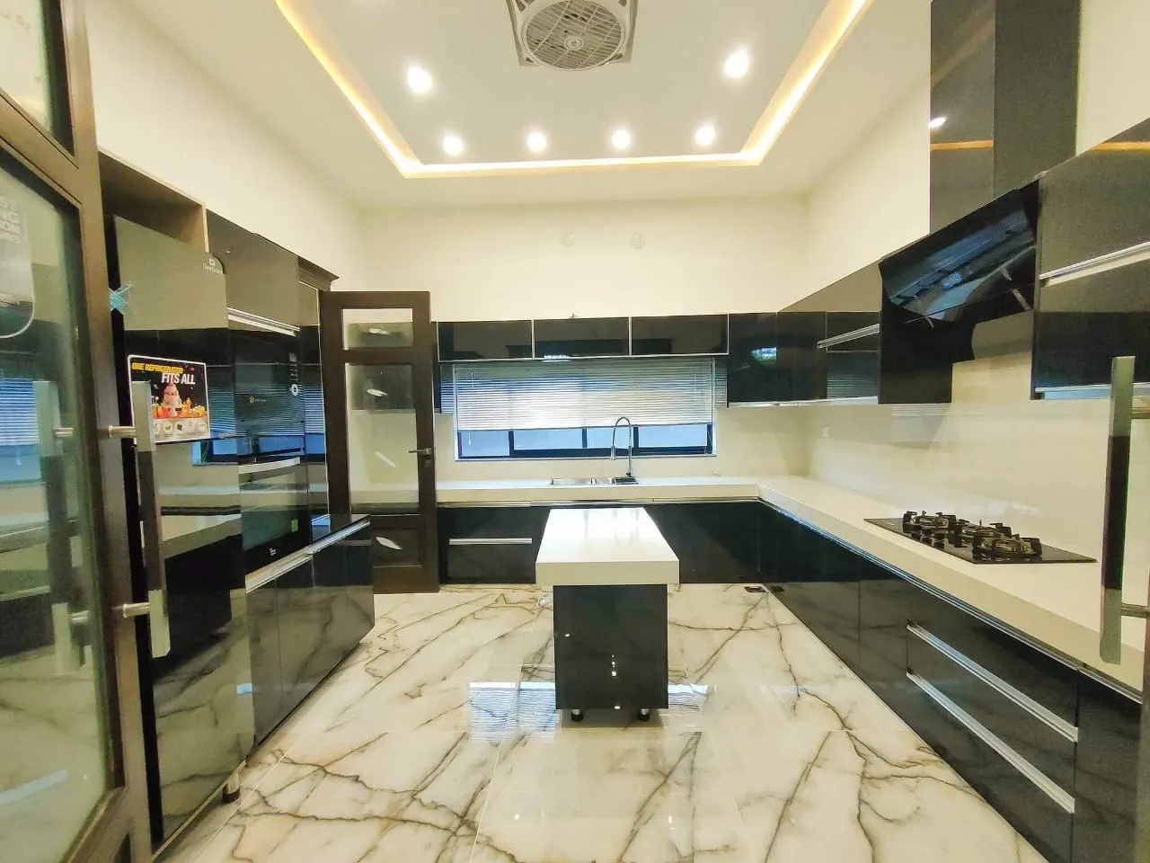 Kitchen with gloss black cabinetry, an island and veined marble flooring